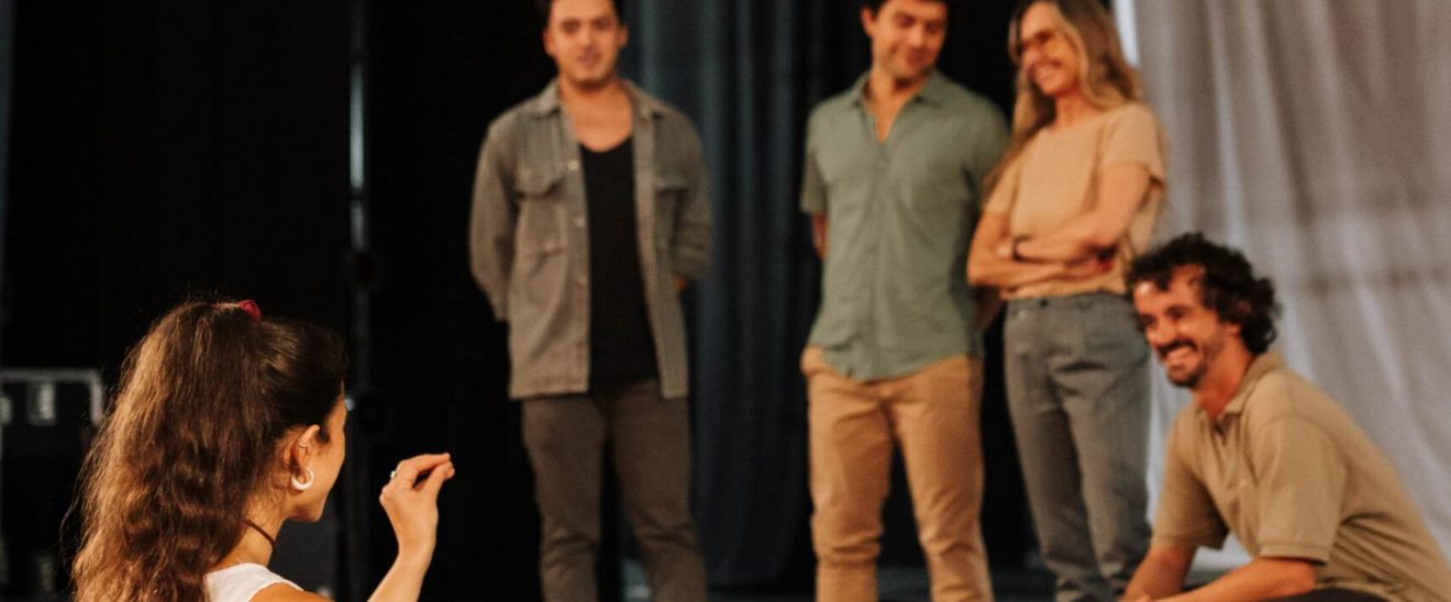 Paula Sanz guía a un grupo de estudiantes en un escenario durante una dinámica de comunicación y trabajo en equipo en escuela de Arte Dramático (Terapia Escénica).