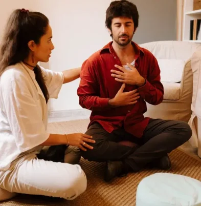 Paula Sanz acompaña a un actor sentado en el suelo con la mano en el pecho, en un ejercicio de regulación corporal (terapia integrativa, Terapia Escénica).